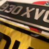 Two custom handmade made number plates, one in black and silver, one in yellow and black