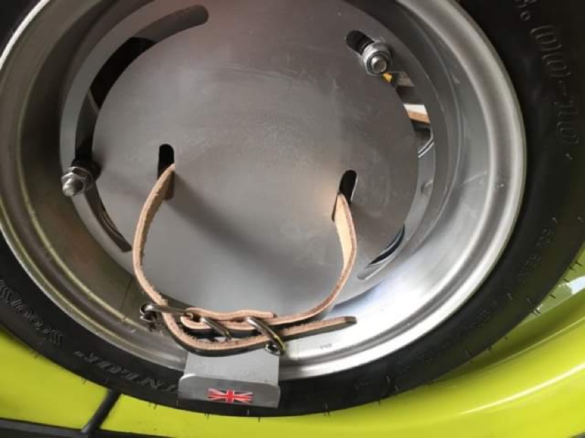 Closeup of spare wheel on a Lambretta Vega showing the strap used to fix a replica oil can to the spare wheel.
