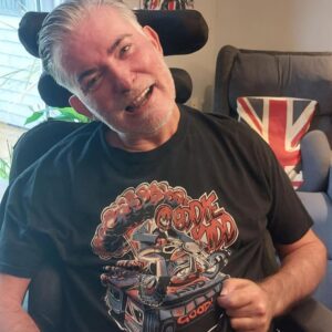 Eddie Kidd wearing a black t-shirt with design showing him on a motorbike riding through the air over some vans.