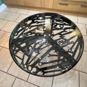 Overhead view of a glass fabricated table with an assortment of spanners inset within it and black powder coated legs