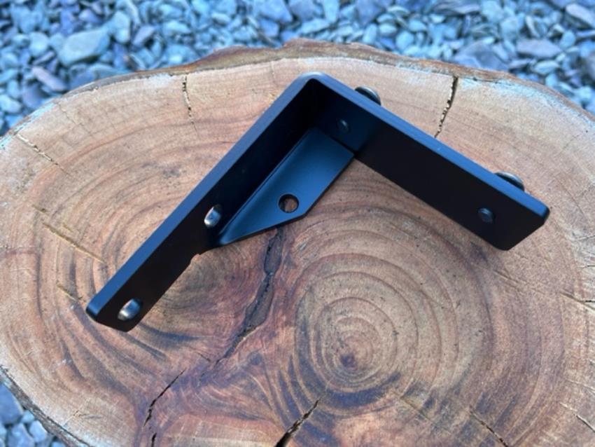 A bracket for a Morris Minor alternator/coil, shown isolated on a piece of wood.