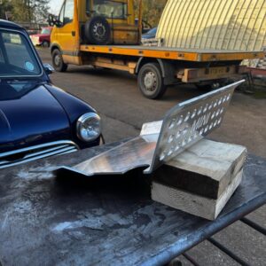 A blue classic Mini car with an aluminium sump guard on a table in front of it.